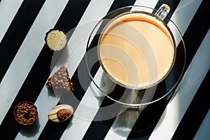 Top view of transparent glass cup of hot coffee with milk and chocolate candies on black and white background