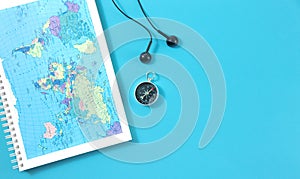 Top view of travel notebook with world map, magnetic compass and headphones on blue background. Space for text