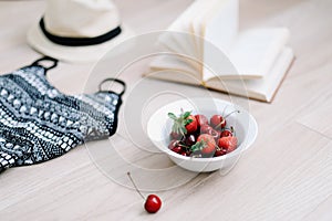 Top view travel or vacation concept. Swimsuit, hat, book and fresh sweet cherries. Flatlay. Summer background.