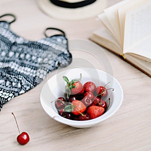 Top view travel or vacation concept. Swimsuit, hat, book and fresh sweet cherries and strawberries.  Flatlay. Summer background.