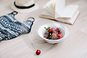 Top view travel or vacation concept. Swimsuit, hat, book and fresh sweet cherries and strawberries.  Flatlay. Summer background.