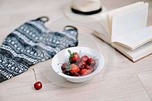 Top view travel or vacation concept. Swimsuit, hat, book and fresh sweet cherries and strawberries.  Flatlay. Summer background.