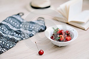 Top view travel or vacation concept. Swimsuit, hat, book and fresh sweet cherries and strawberries.  Flatlay. Summer background.