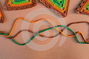 Top view of tree crochet cords and parts of multicolored crochet motifs on beige background.