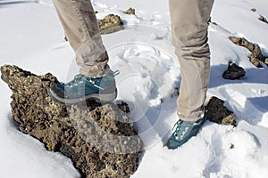 top view of trekking shoes on the lava stone and snow background, female legs