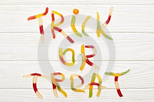 Top view of trick or treat lettering made of colorful gummy sweets on white wooden table with spiders, Halloween treat.