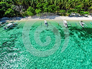 Top view of a tropical island with palm trees and blue clear water. Aerial view of a white sand beach and boats over a coral reef