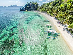 Top view of a tropical island with palm trees and blue clear water. Aerial view of a white sand beach and boats over a coral reef
