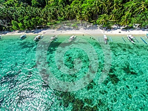 Top view of a tropical island with palm trees and blue clear water. Aerial view of a white sand beach and boats over a coral reef