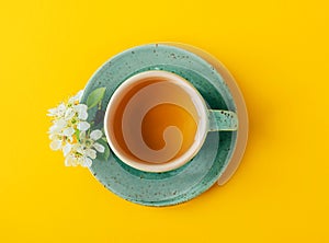 Top view of turquoise cup of green or herbal tea on saucer with spring tree flowers over bright yellow background