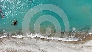 Top view of turquoise Mediterranean Sea waters rolling on pebbles. Aerial view of transparent foamy waves splashing on