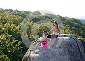 Top view of two attractive athletic barefooted girls sitting in lotus pose on top of huge rocks