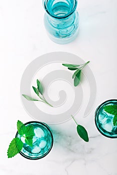 Top view of two beautiful vintage turquoise glasses and a bottle with cold drink and ice cubes, decorated with fresh green mint
