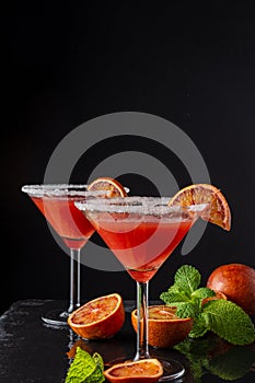 Top view of two blood orange martini glasses, half orange and mint, on black background, vertical