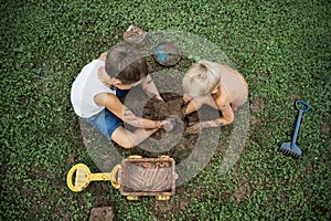 Top view of two brothers sitting on  grass playing with mud