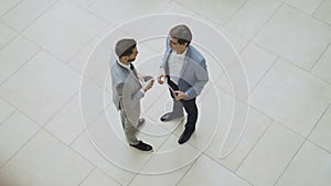 Top view of two businessmen greeting and shaking hands and chatting during coffee break in lobby of business center