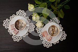 Top view of two cups of coffee with milk, Turkish delight on a saucer, white roses.