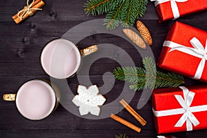 Top view of two cups of hot cocoa, ginger snowflake cookie, red gift boxes and fir tree branches on wooden background.