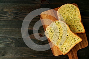 Top View of Two Delicious Homemade Garlic Butter Toasts on Breadboard Served on Dark Brown Table