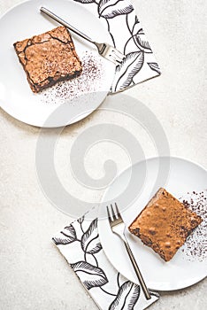 Top view of two dessert plates with brownie cake over white rustic background