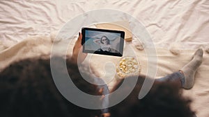 Top view of two girlfriends sitting on bed at home talking on skype on tablet computer with their friend having vacation