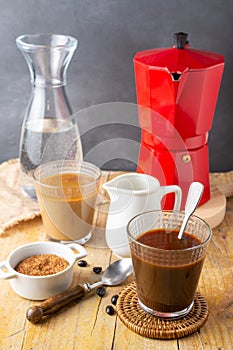 Top view of two glasses with ice coffee, spoon, coffee beans, brown sugar, milk jug with red coffee pot and bottle of water, with
