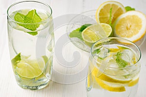 Top view of two glasses of water with lemon and lime slices with ice cubes on white wood