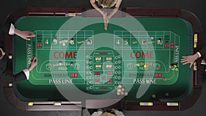 Top view of two men and a woman playing craps while sitting at a table in a casino. Players place bets with chips. The