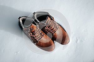 Top view of two new men's leather brown winter boots standing in snow on sunny day, outdoors. Shoes for hiking and traveling