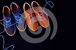 Top view of two pairs of suede sneakers with neon laces on black background