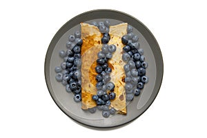Top view of two pancakes with fresh blueberries on grey plate isolated on white background