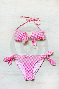 Top view of two pieces pink chequered swimming suit over wooden background.