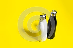 Top view of two reusable eco, steel stainless, thermo water bottle, white and black color, isolated on yellow background.