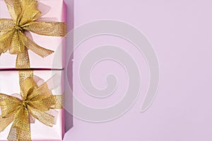 Top view of two small wrapped gift boxes with golden bows on pink background, copy space for text