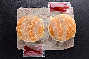 Top view of two tasty homemade burgers on paper and ketchup on black background