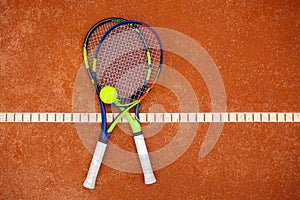 Top view of two tennis rackets and yellow tennis ball lie on the clay court