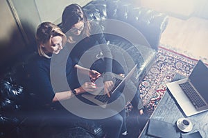 Top view of two young girls working on computer and using mobile devices at modern loft.Woman wearing black pullover and