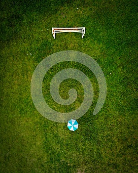 Top view of umbrella and goal on the green field. Minimalist drone shot goals conceptual.