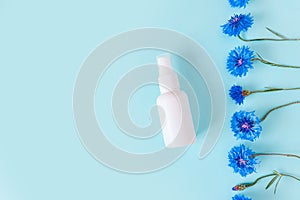 Top view of unbranded white plastic spray bottle mockup and Flower line of blue cornflowers on a pastel blue background.