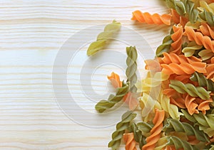 Top view of uncooked three-color fusilli pasta on natural wooden table, with free space for text