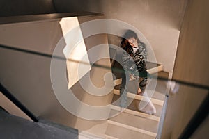 Top view of unhappy pensive female in casual clothes with apathy expression sitting alone on stairs. High-angle view of