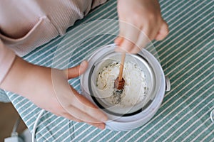 Top view of unrecognizable female artisan craftperson mixing dry soy wax for creating candle building mixture. Process