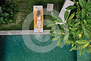 Top view of unrecognizable slim young woman in beige bikini relaxing and sunbathe near luxury swimming pool in green