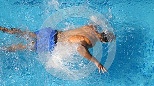 Top view of unrecognizable sporty man jumping in clear blue water of pool. Young muscular guy floating across the basin