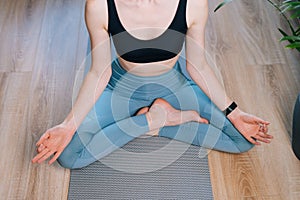 Top view of unrecognizable young woman meditating at home sitting in lotus position on yoga mat