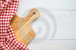 Top view of unused brand new brown handmade wooden cutting board and red napkins on white wooden table background - Food and kitch