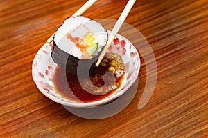 Top-View of using chopsticks hold Futomaki Sushi dip in soy sauce and wasabi