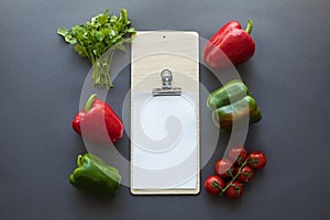 Top view of various fresh peppers, tomatoes, parsley and blank paper sheet with cutting board