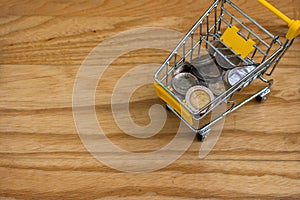 Top view of various money coins Baht in yellow mini shopping cart or supermarket trolley.