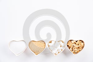 Top view of various types of sugar. Cube sugar, raw sugar brown sugar and granulated sugar in heart bowl on white background. Flat